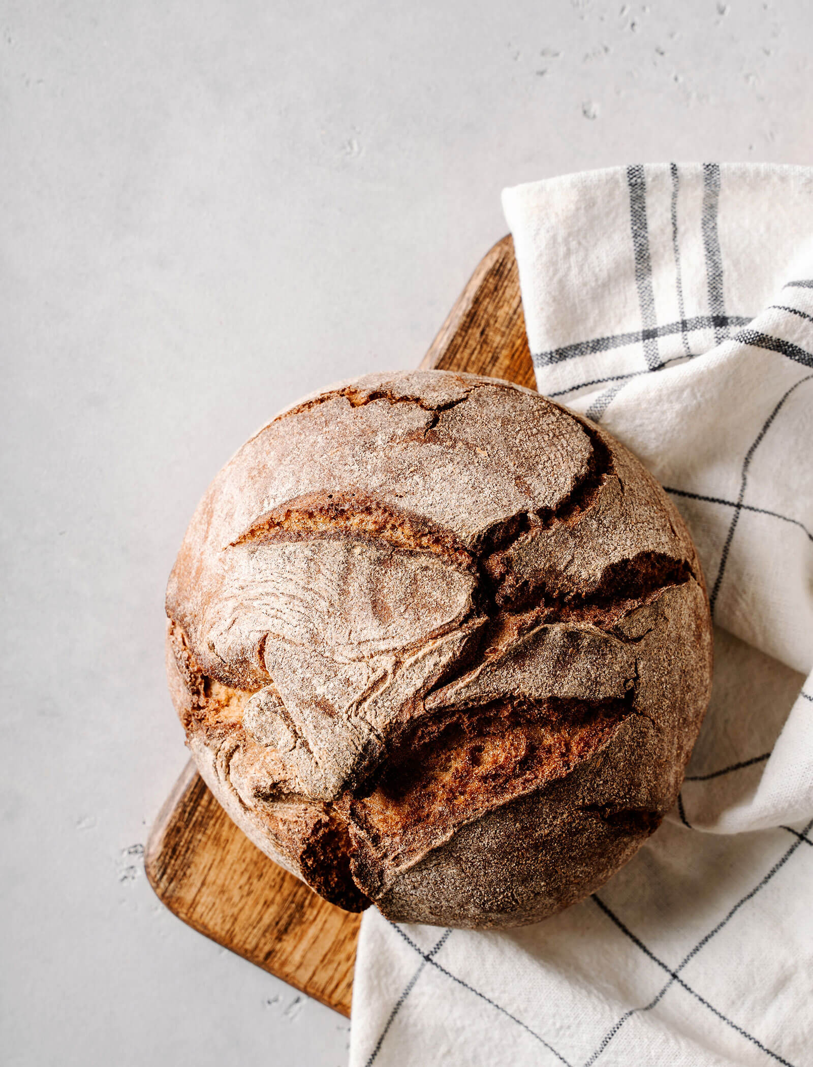 Pane rustico rotondo su una tavola di legno, parzialmente coperto da un telo da cucina bianco e a righe. - AMIL chalets dolomites