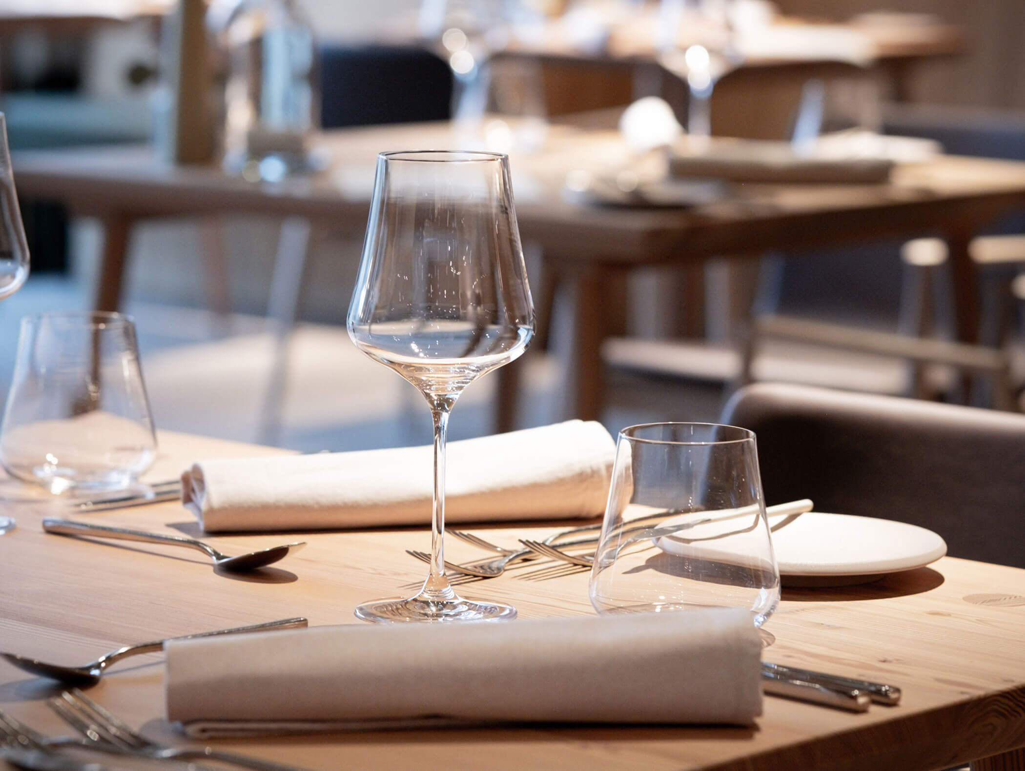Primo piano di un tavolo da ristorante elegantemente apparecchiato con bicchieri, piatti e tovaglioli bianchi arrotolati. - AMIL chalets dolomites