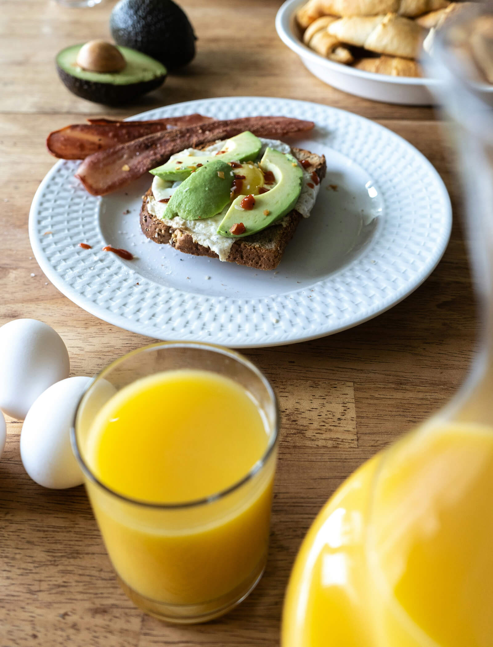 Una colazione a base di avocado toast, bacon, uova e un bicchiere di succo d'arancia su un tavolo di legno. - AMIL chalets dolomites
