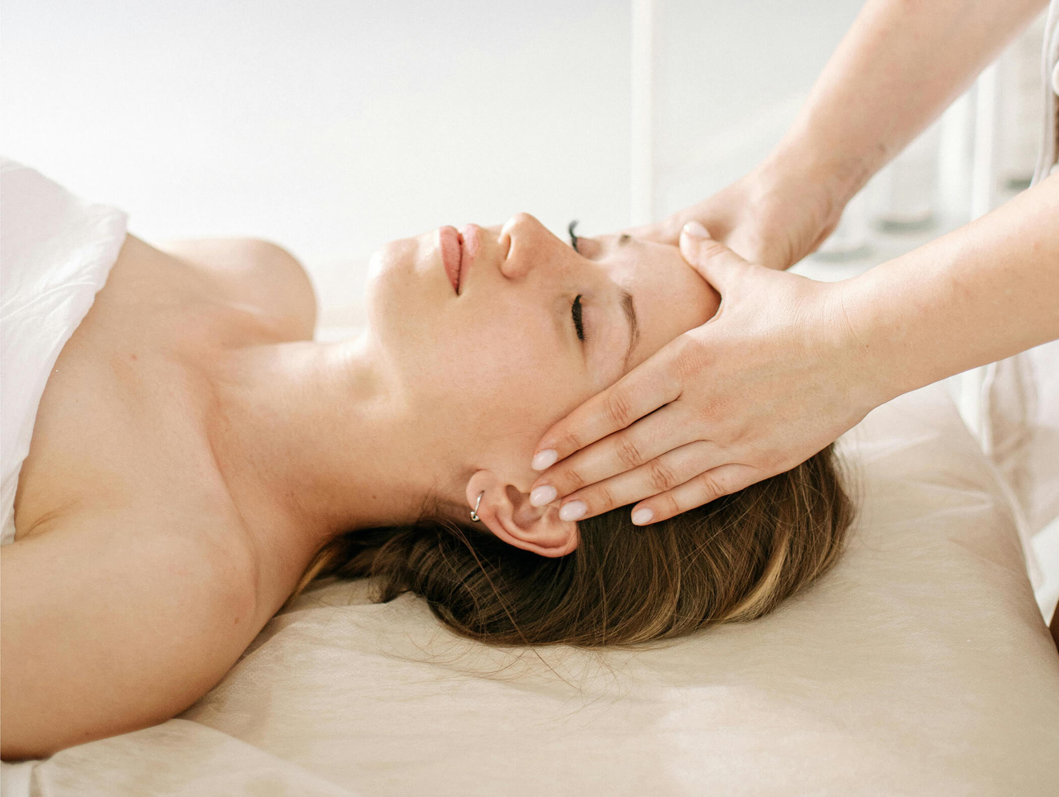 A woman lying down with eyes closed, receiving a relaxing head massage from a person. - AMIL chalets dolomites