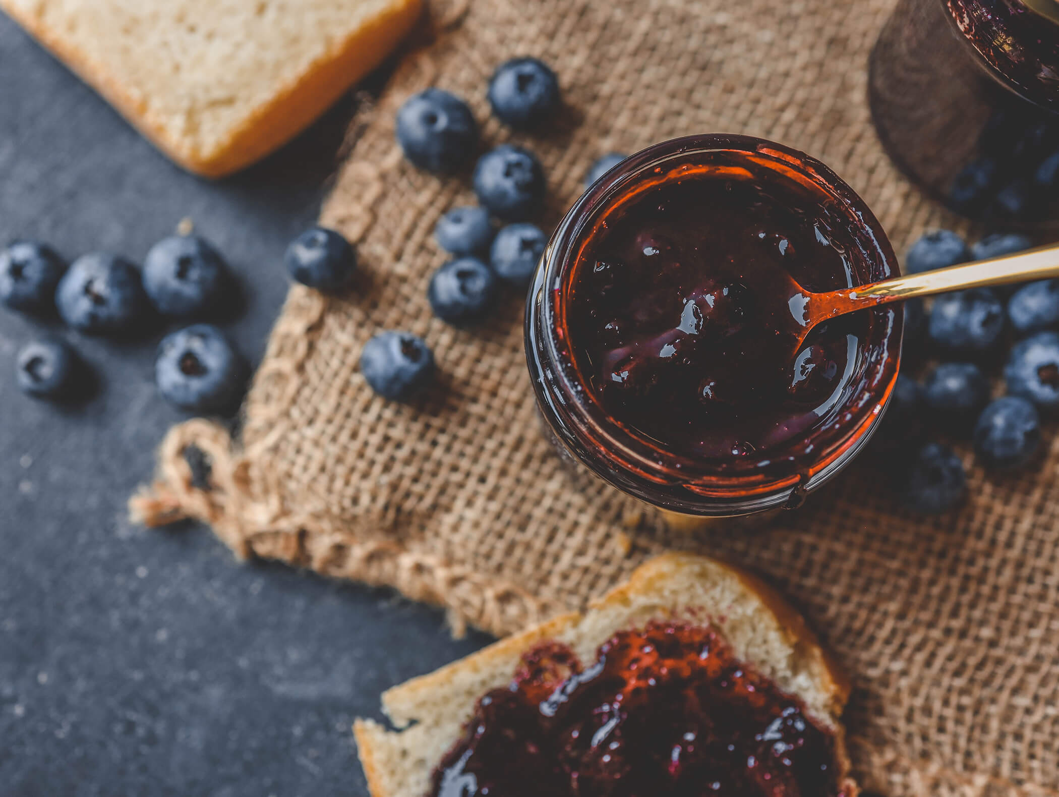 Un barattolo di marmellata di mirtilli con un cucchiaio, mirtilli freschi e pane su un telo di iuta. - AMIL chalets dolomites